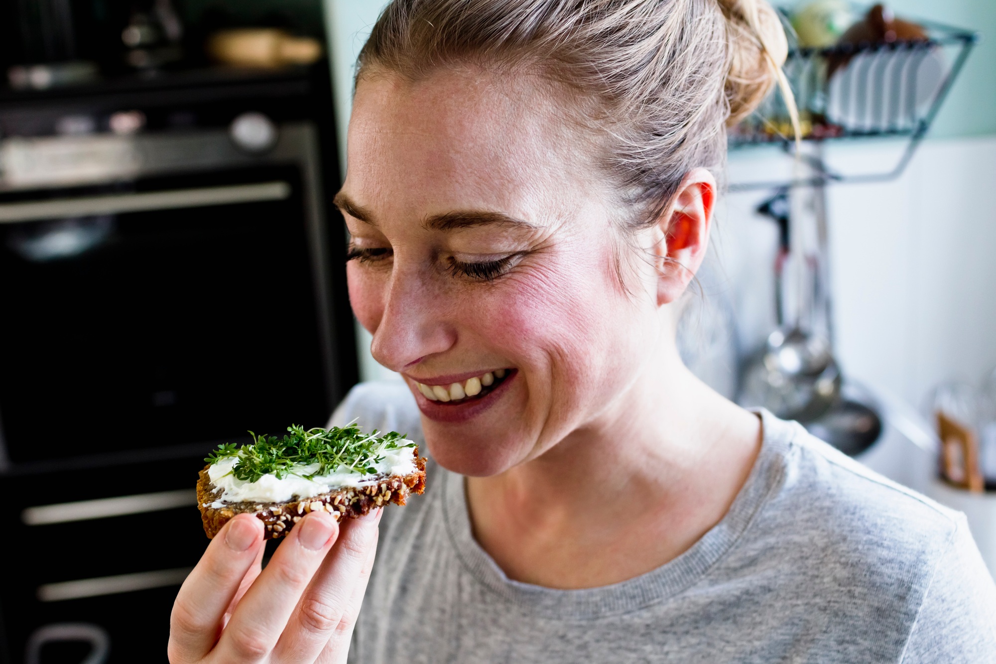 Mid adult woman eating rye bread snack in kitchen