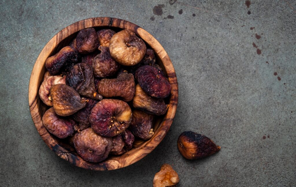 Organic sun dried figs in bowl on green background, top view