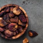 Organic sun dried figs in bowl on green background, top view